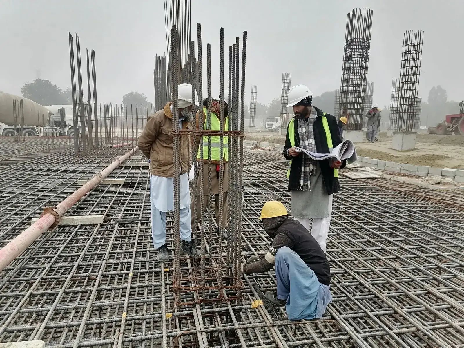 Obra em andamento com ferragens de concreto armado e trabalhadores no canteiro
