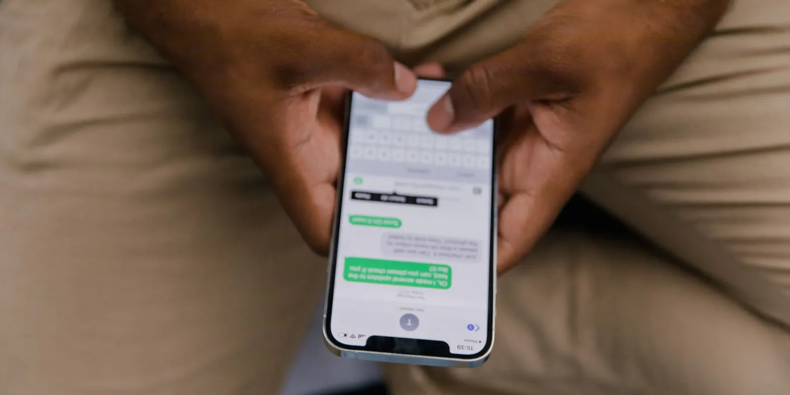 Homem sentado segurando o celular com as duas mãos, com uma conversa aberta na tela